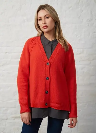 studio shot of blonde woman wearing bright red cardigan with grey collared shirt underneath